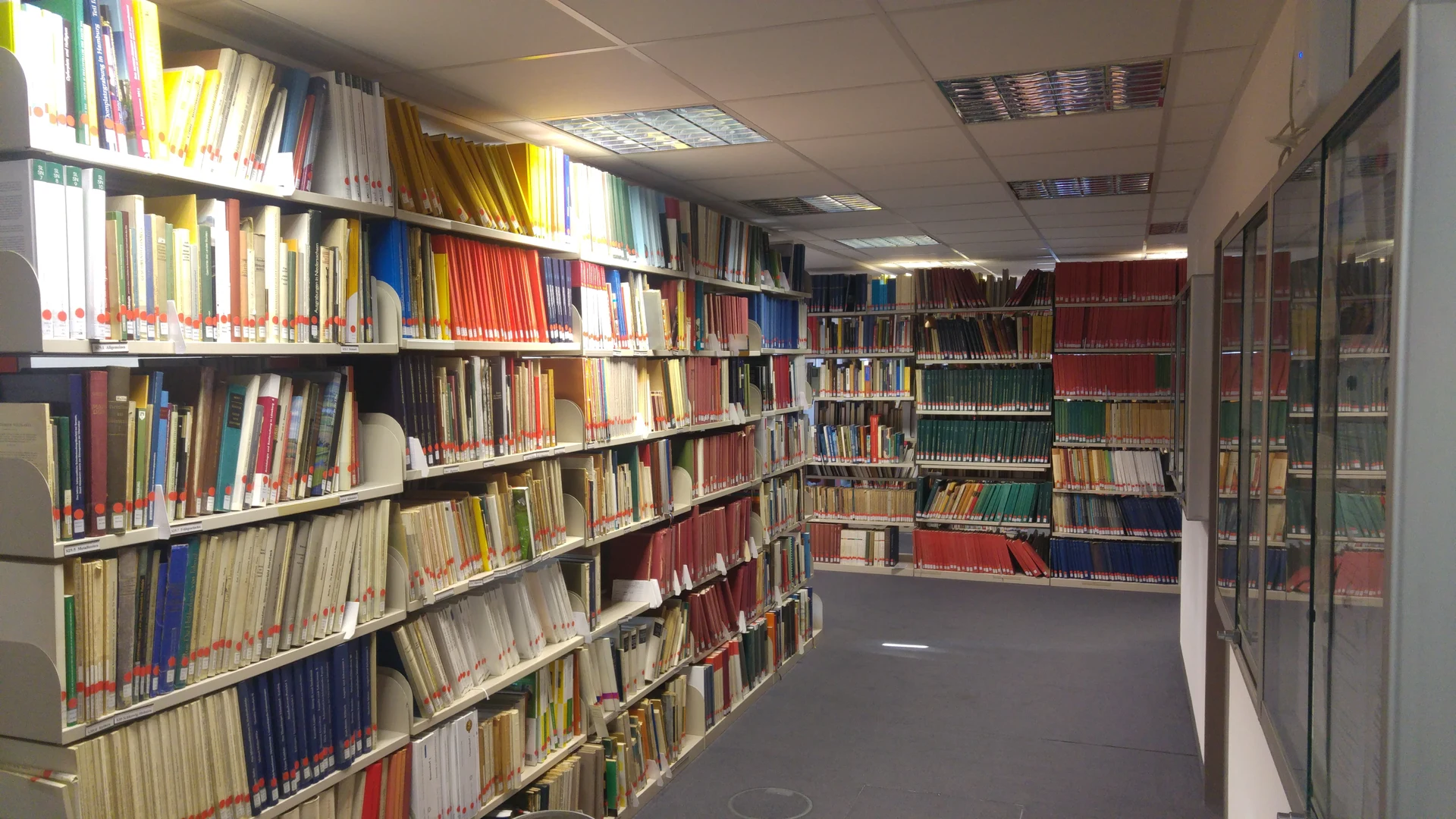 Eine Wissenschaftlerin und ein Wissenschaftler arbeiten hinter einer Glasfassade und mischen Chemikalien mit Großgeräten.