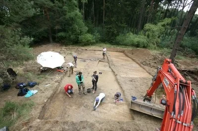 Eine Wissenschaftlerin und ein Wissenschaftler arbeiten hinter einer Glasfassade und mischen Chemikalien mit Großgeräten.